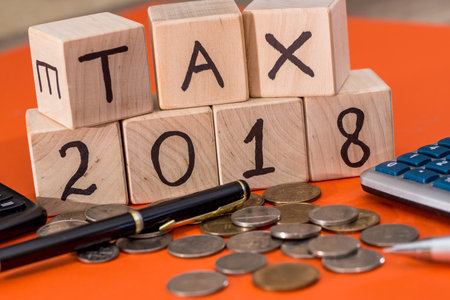 tax 2018 wooden cubes with coin, pen and calculator isolated on orange
