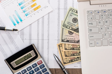 Dollar bills on a table with graph chart and laptop, pen and calculatorの写真素材