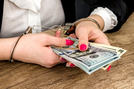 women's hands in handcuffs with dollars in their handsの写真素材