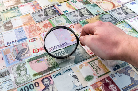 Male hand with magnifier checking world banknotesの写真素材