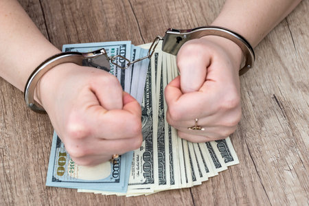 Female hands in handcuffs on dollar banknotesの写真素材