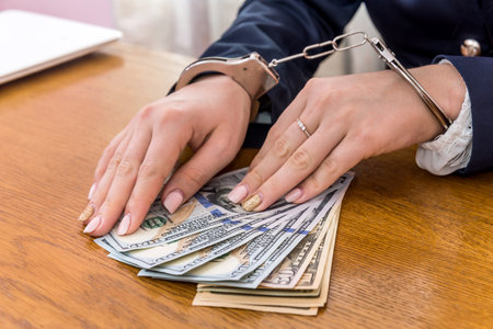 Female hands in handcuffs on dollar bribeの写真素材