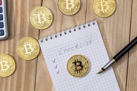 Bitcoin with checklist on a notepad with pen and calculatorの写真素材