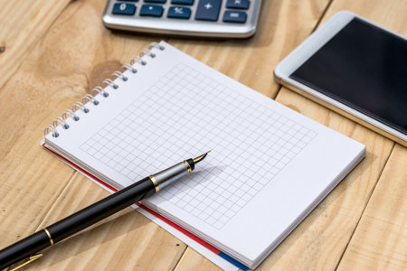 Smartphone with notebook, pen and calculator on wooden table