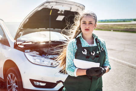 Woman mechanic with clipboard standing near broken car