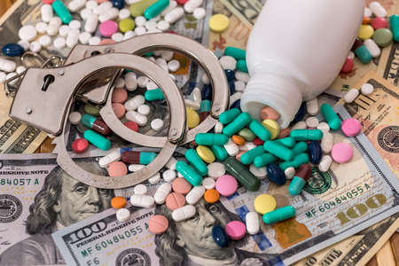 Dispersed pills from container with handcuffs on dollar banknotesの写真素材