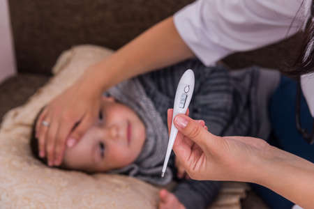 Female hand with thermometer and sick little boy