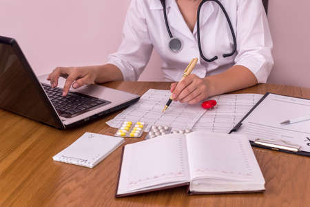 Doctor at workplace, typing on laptop and pointing on cardiogramの写真素材