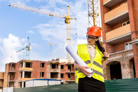 Woman engineer in helmet with rolls on construction site