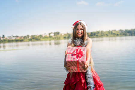 Beautiful girl santa holding gift box on seashoreの写真素材