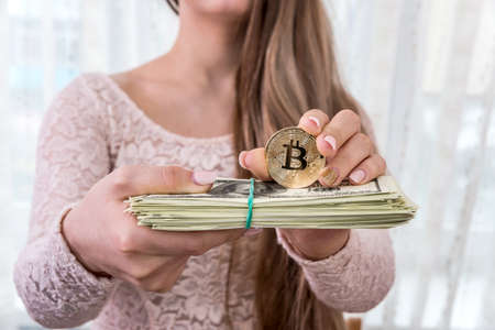 Young woman showing bundle of dollars and golden bitcoinの写真素材