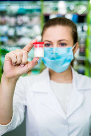 Woman apothecary looking at container with tablets in drugstoreの写真素材