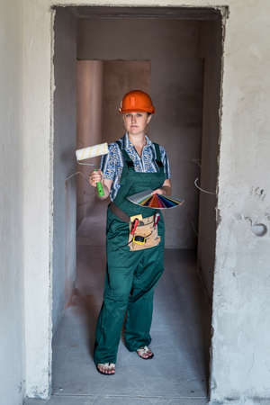 Woman builder in uniform holding painting roll and color swatchの写真素材