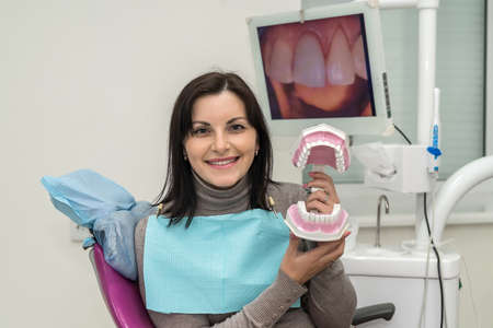 Woman in dentist chair holding jaw and smilingの写真素材