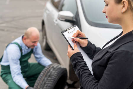 Woman filling document while mechanic changing wheelの写真素材