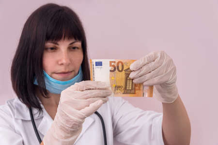 Doctor looking at fifty euro banknote holding it in glovesの写真素材