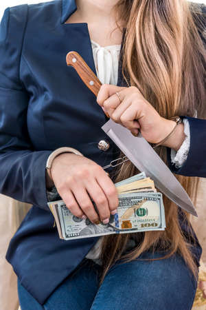 Female hands in handcuffs with knife and dollarの写真素材