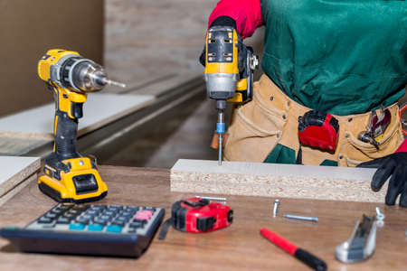 Carpenter with screwdriver constructing furniture in carpentry