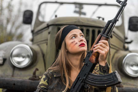 Woman with rifle posing on military car