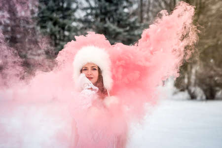Beautiful woman in winter park holding red smoke bomb