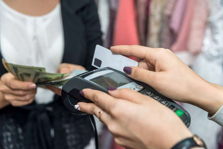 Payment in clothes store with terminal, credit card and cash