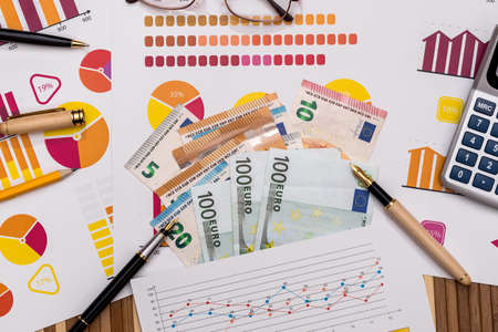 Euro banknotes on business graphs with calculator and pen