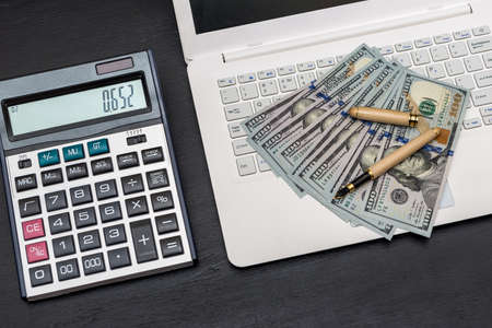 Laptop with dollar banknotes on black background