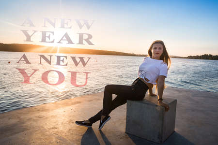 Slim woman posing on lake shore sitting on stone
