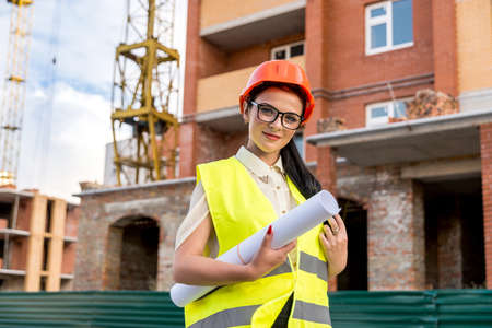 Beautiful architect with blueprints in rolls on construction site