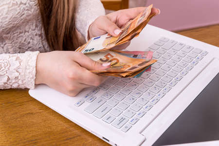 Hands of businesswoman counting euro banknotes on laptop keyboardの写真素材