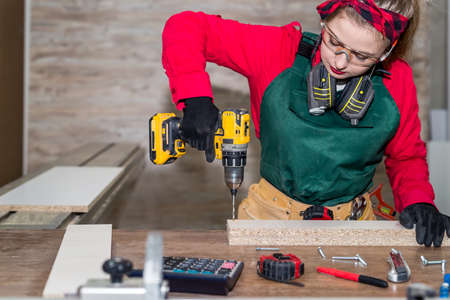 Woman carpenter making hole in wooden plankの写真素材