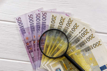 Euro banknotes with magnifying glass on table