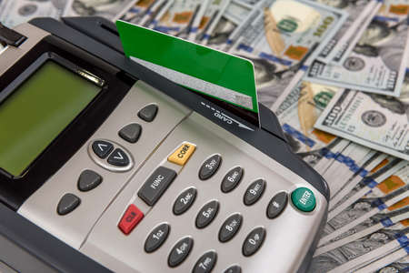 Banking terminal with green credit card and dollar background