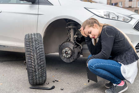 Woman in despair looking at spare wheel for carの写真素材