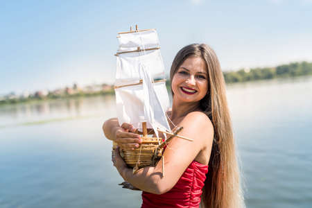 Woman in red dress holding boat model on the beachの写真素材