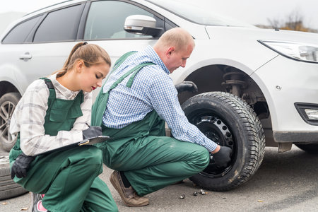 Woman inspecting how mechanic fixing car wheelの写真素材