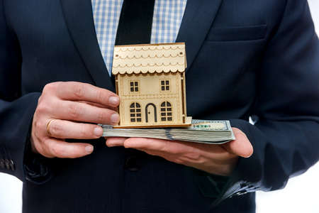Man holding wooden house model and dollar banknotesの写真素材