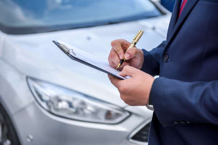 Male hands with clipboard against new car