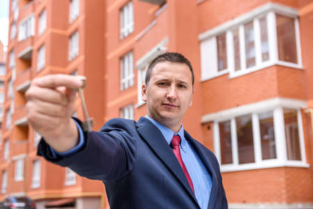 Agent in suit showing key near new buildingの写真素材