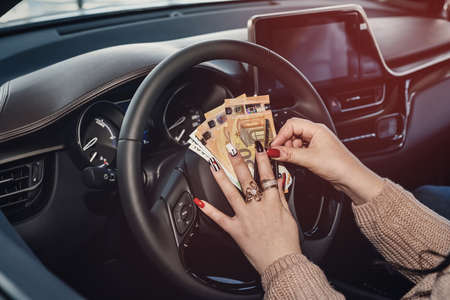 Woman driver holding euro banknotes and keys on steering wheel