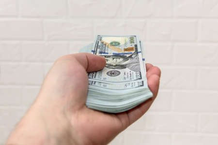 Hand with dollars pile close up on wall brick background