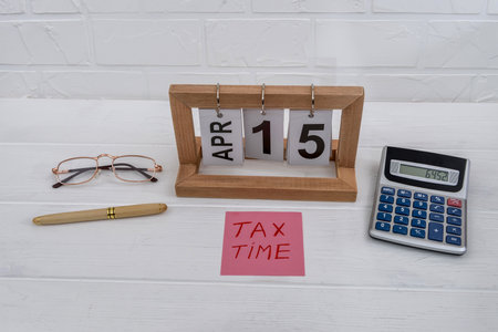 Tax time with wooden calendar, calculator, glasses and penの写真素材
