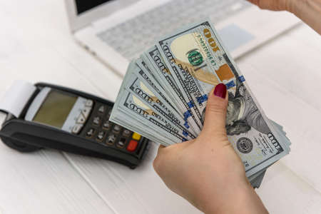 Female hand holding dollar banknotes against laptop and terminal