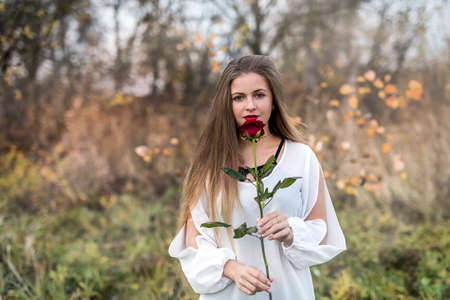 Beautiful young woman with red rose posing outdoorsの写真素材