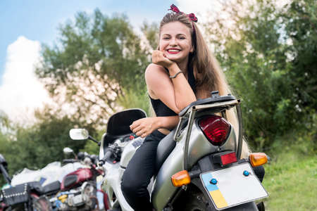 Beautiful girl with long hair posing at a motorcycleの写真素材