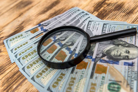Hundred dollar banknotes with magnifying glass on wooden backgroundの写真素材