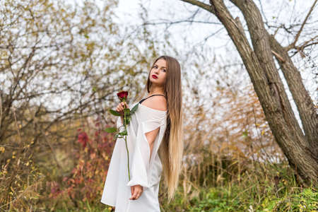 Beautiful young woman with red rose posing outdoorsの写真素材
