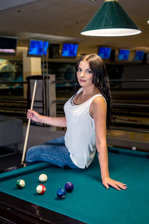 Brunette woman with cue near billiard table