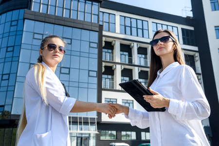 Partnership. Two young business ladies handshaking outside office building