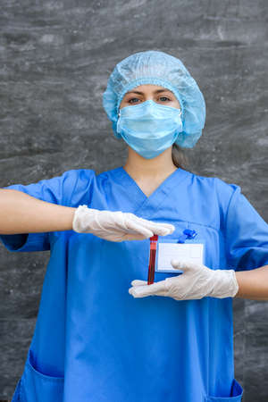 Women in medical uniform posing with test tubes with red substance on gray background